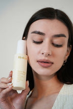 Woman holding a Hysken skincare product against a neutral background