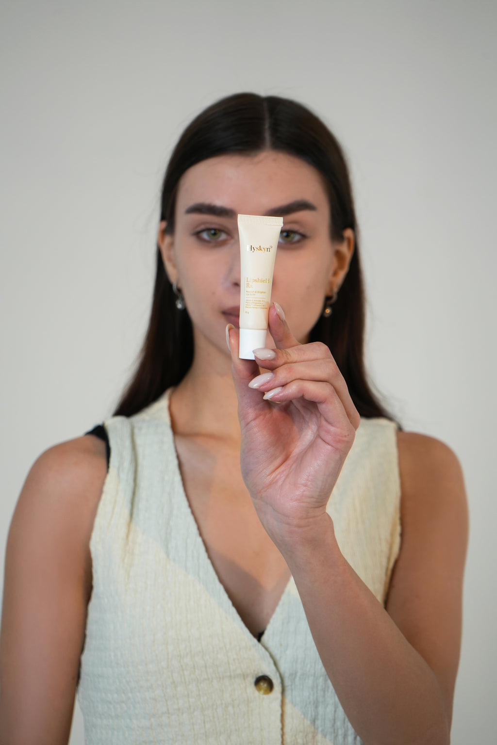 Woman holding a skincare product against a plain background