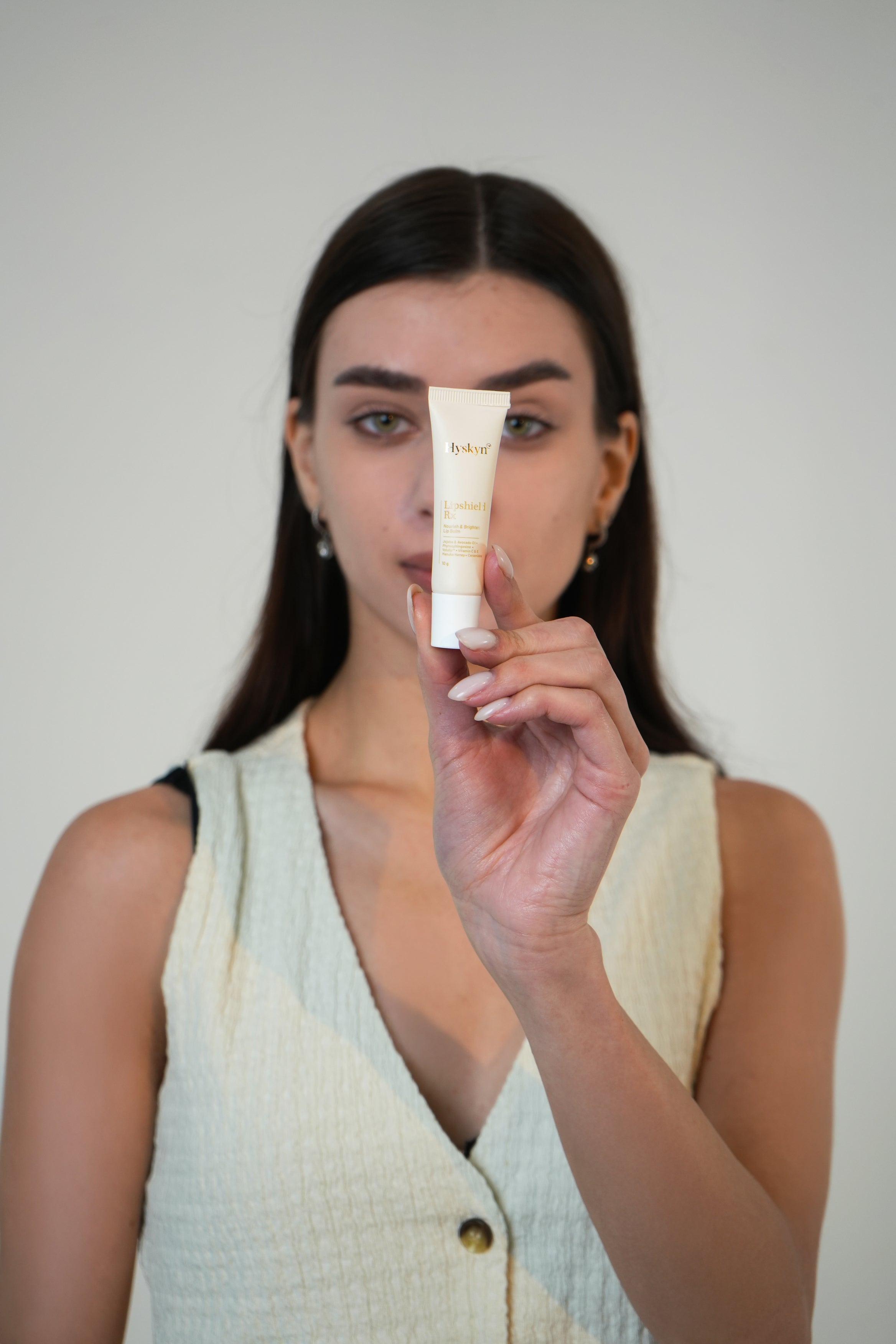 Woman holding a skincare product against a plain background