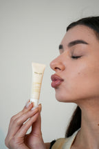 Woman holding a skincare product close to her face against a plain background