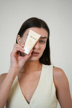 Woman holding a tube of hydrating sunscreen product against a plain background