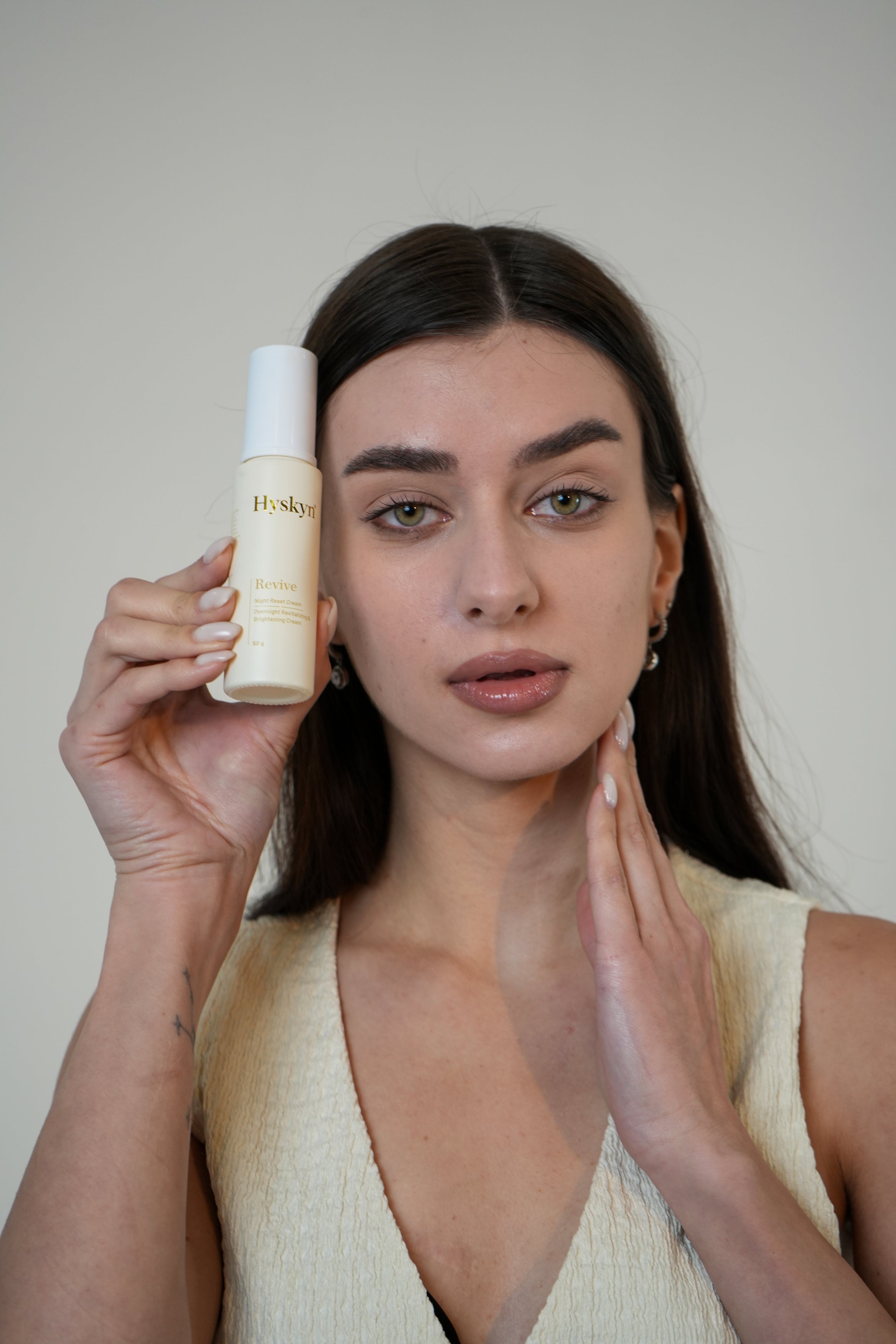 Woman holding a skincare product with a neutral background