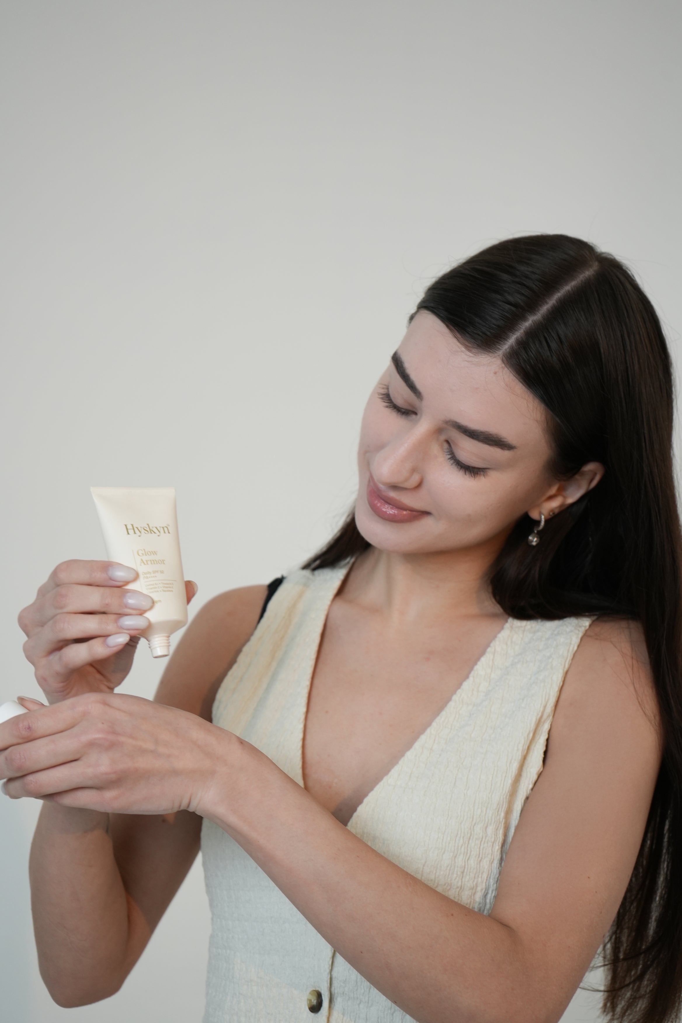 Woman holding a skincare product against a plain background